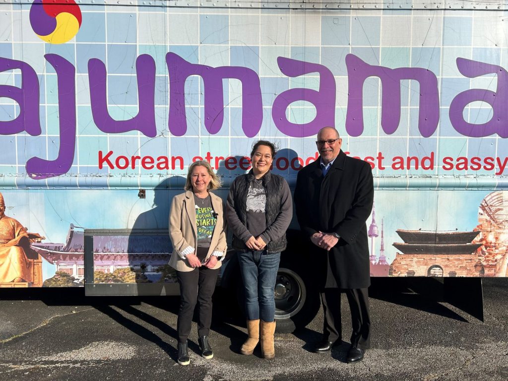 Three people standing in front of the Ajumama Korean food truck.