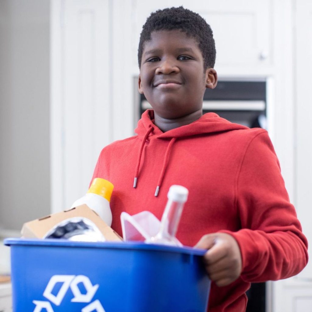 A boy carrying a recycling bin.