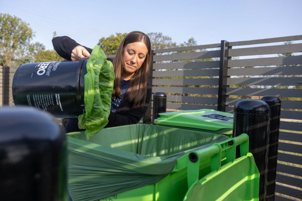 A woman pouring a bucket of recyclables into a larger bin.