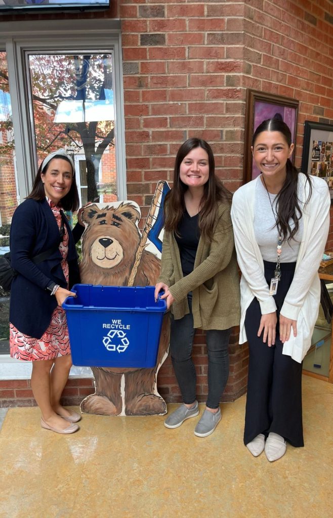 Three elementary school teachers, two of which are holding a recycling bin.