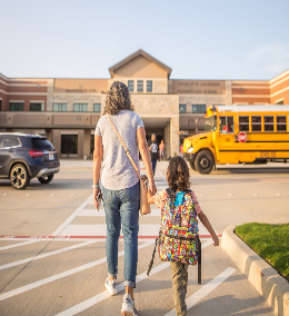 A little girl being walked to the bus by her mother