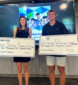 Two college students holding giant checks