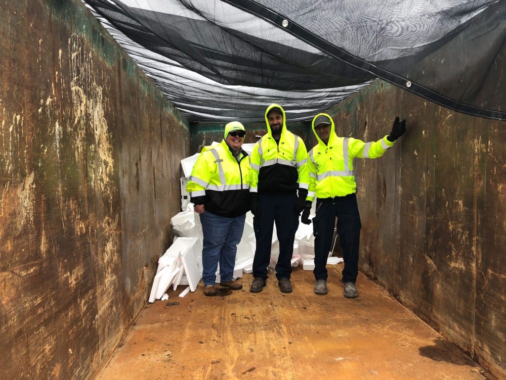 Three people in yellow jackets with styrofoam behind them.