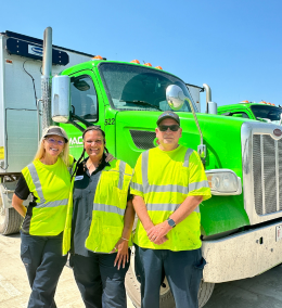 Three people in yellow vests in front of a truck.