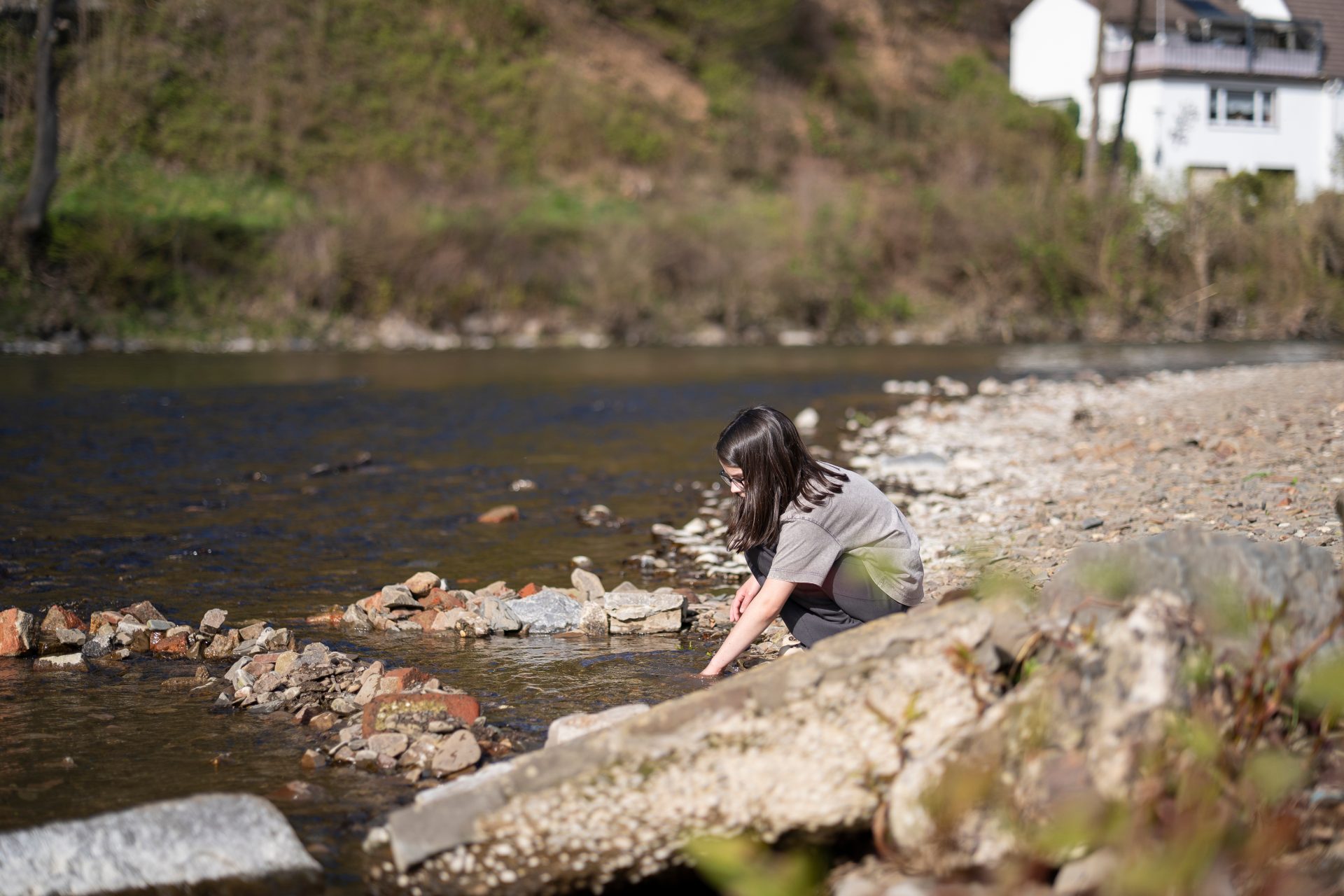Child playing with stones on a shallow riverbank in natural sunlight. Concept of curiosity and connection with nature