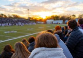 Exciting High School Football Game Unfolds at Sunset With Cheering Fans