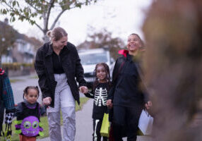 Woman with children in Halloween costumes walking on sidewalk